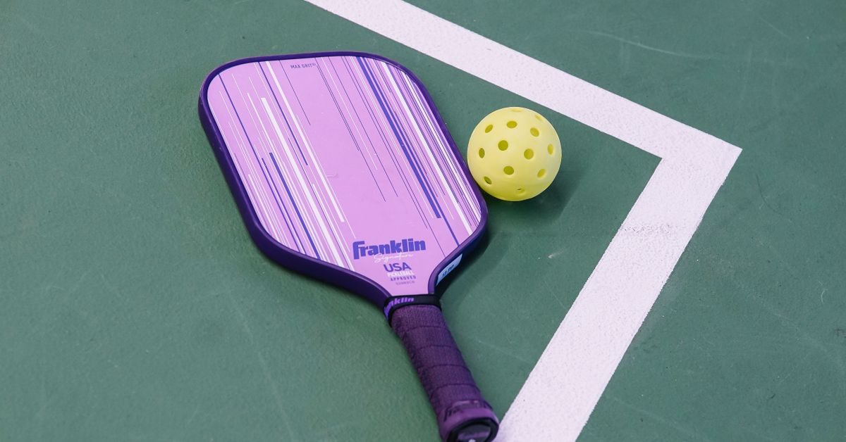 Pickleball paddle and ball resting on an outdoor court