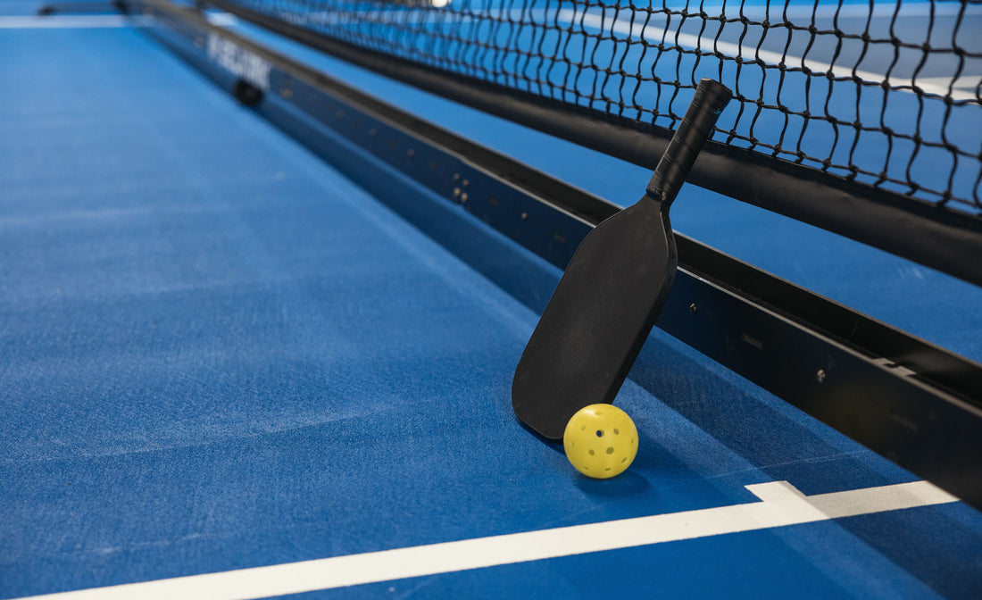 Pickleball paddle and ball resting next to the net on court