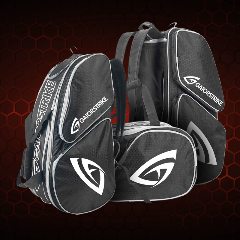 An orange and blue sports bag with “GAMOSTRIKE” branding stands behind two baseball caps, one white with a green logo and one pink with a gray logo, both matching the bag’s style.