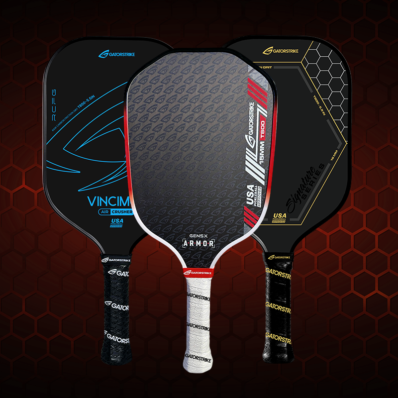 Three pickleball paddles stand upright side by side. Each paddle has a unique design: one is red and gray, one is black with gold text, and one is black with blue accents. All have white handles.