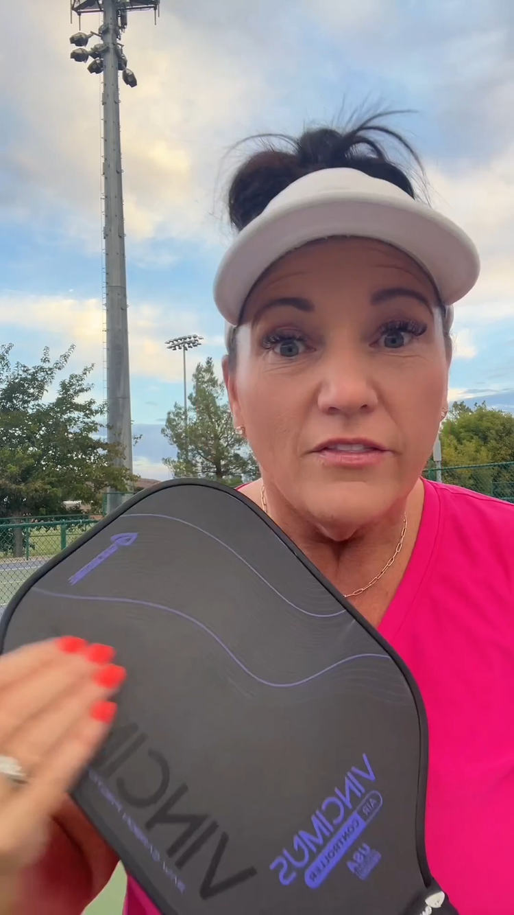 Woman in a pink shirt and white visor holds a black pickleball paddle outdoors, ready to consult the pickleball rules PDF.