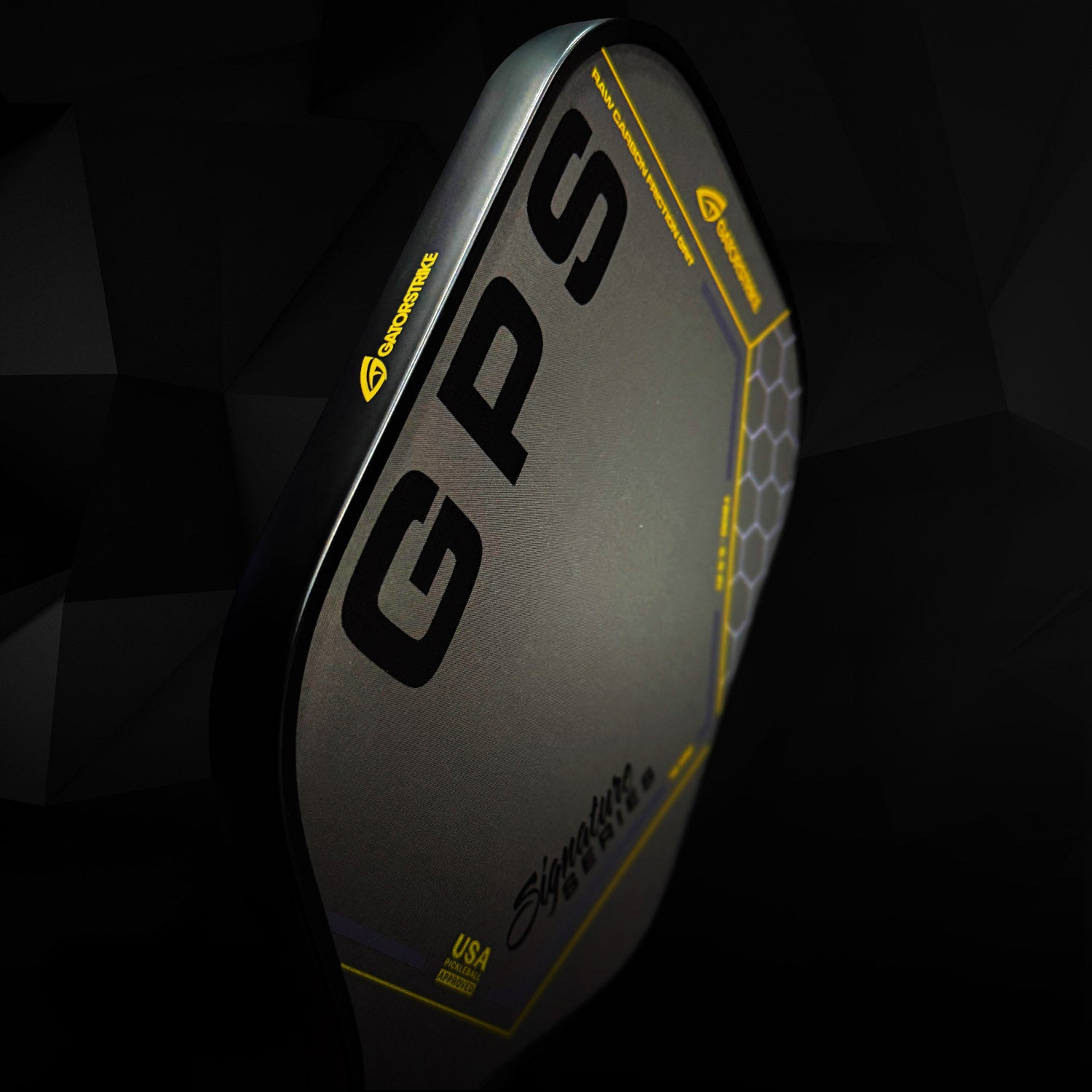 A close-up of a black carbon fiber GATORSTRIKE pickleball paddle with “GPS” in bold letters, a honeycomb hexagon pattern, yellow accents, and “Signature” in script near the anti-vibration foam handle.