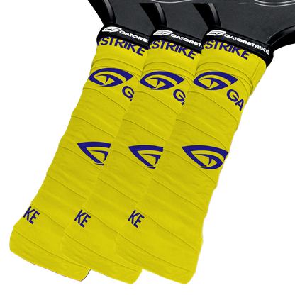 Three overlapping yellow GATORSTRIKE sports paddle overgrips with a blue alligator-eye logo and black tops displaying the white GATORSTRIKE label, designed for a secure hold, are shown against a white background.