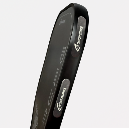 Black rectangular kick pad angled upward, features paddle weights for stronger swings and white “GanoStrike” logo on handles.