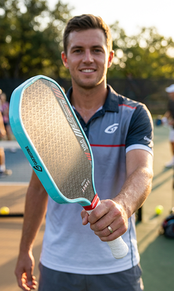 Smiling man on a court holds a GatorStrike pickleball manual, wearing a sporty shirt.