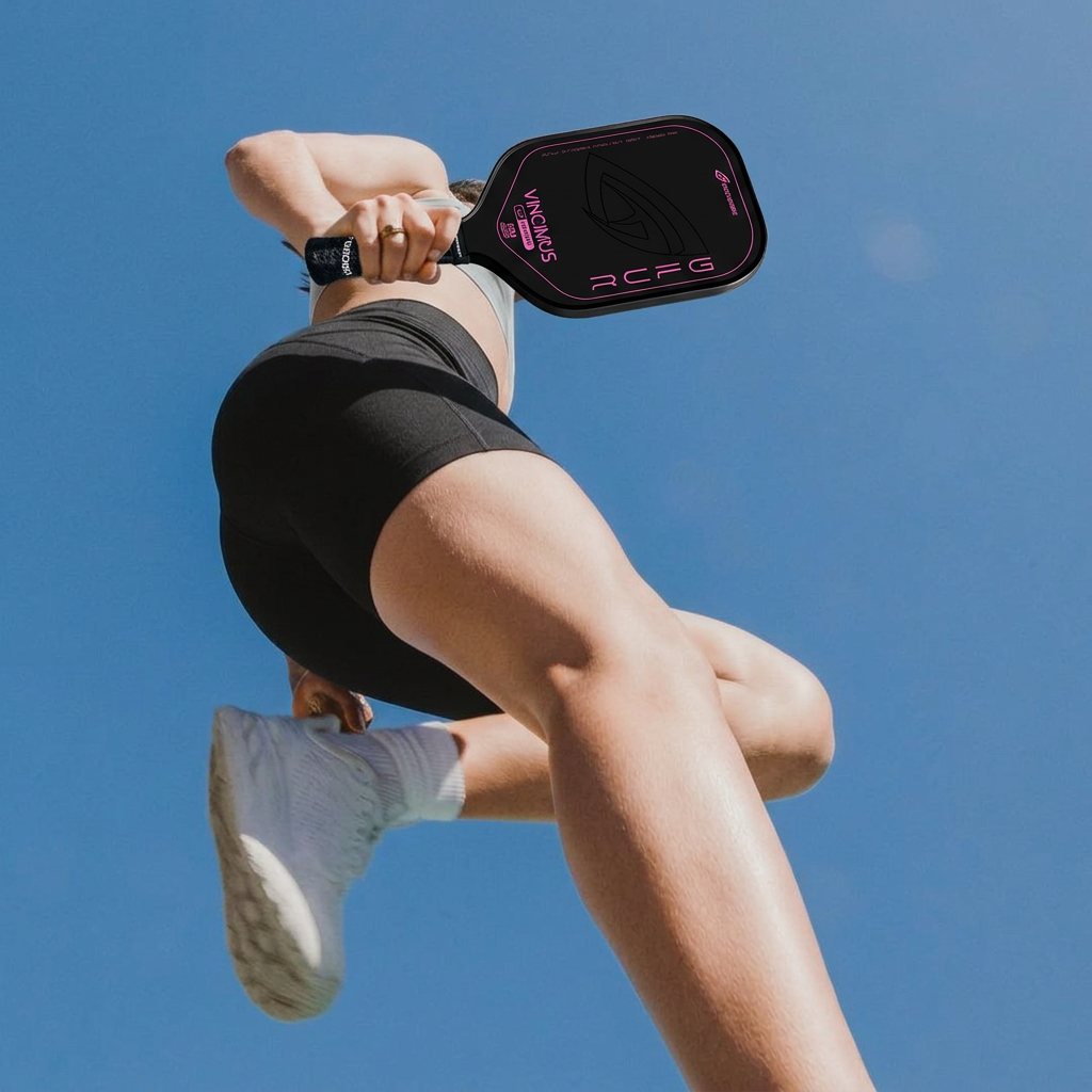 Woman in athletic wear holding a GatorStrike pickleball manual, photographed from below against a clear blue sky.